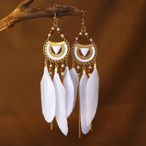 Bohemian long white feather earrings with gold leaf accents on a rustic wood branch
