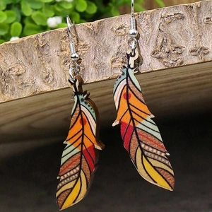 Detail showing bohemian feather earrings with vibrant patterns hanging on wood