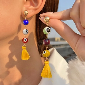 Detailed close-up of beaded evil eye earrings with vibrant yellow thread tassels