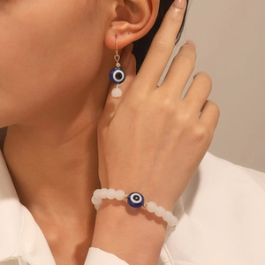 Detalle de modelo luciendo pendientes de ojo turco azul y pulsera de cuentas blanca