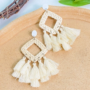 Detailed macro view of bohemian woven raffia earrings with cream white tassels and sunflower style