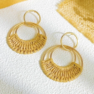 Detail of woven raffia drop earrings with gold metal rings and bohemian vintage texture