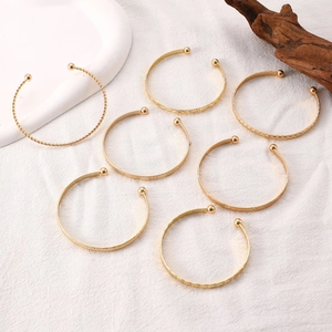 Detail of 7-piece gold-plated open cuff bracelet set with textured patterns on linen cloth
