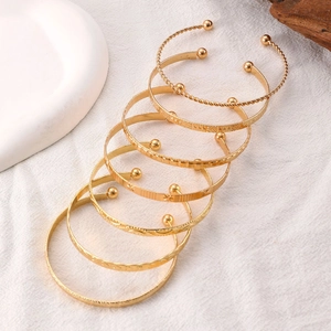 Detailed view of six gold-plated vintage textured open bangles on a decorative setup