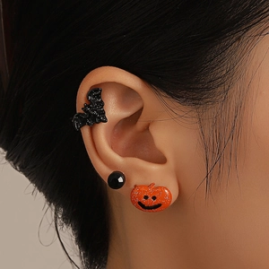 Macro shot of Halloween jewelry set featuring black bat ear cuff and pumpkin face stud
