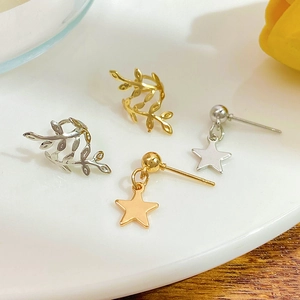 Set aus Stern-Ohrhängern und Blatt-Ohrklemmen in Gold und Silber auf weißer Keramik