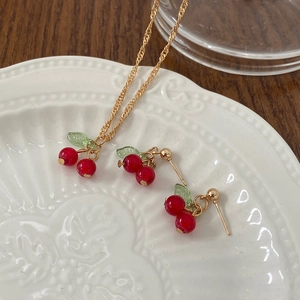 Close-up of cherry necklace and earrings set with red beads and green leaves on white plate