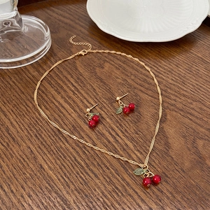 Macro shot of gold tone cherry necklace and earrings set on an elegant rustic table