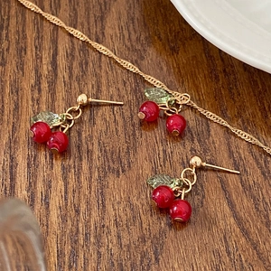 Elegant cherry pendant necklace and earring set with red beads and green leaves on wood