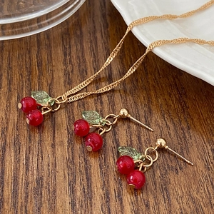 Macro shot of cherry necklace and earrings set with red pendants on a wooden table