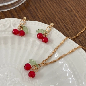 Macro view of cherry necklace and earring set on a vintage white ceramic platter