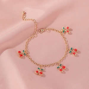 Detailed view of gold cherry bracelet with five red enamel charms on pink satin