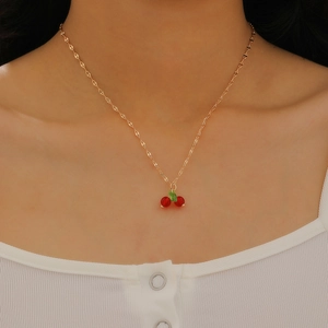 Close-up of elegant cherry necklace with red beads and green leaves on a gold chain