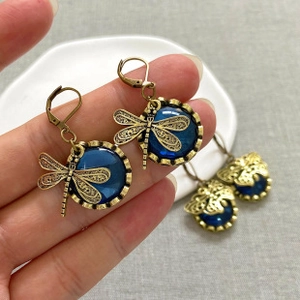 Detailed close-up of retro dragonfly drop earrings with blue resin stones and gold plating