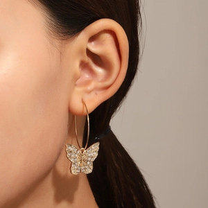 Detail view of a gold hoop earring with a sparkling crystal butterfly pendant on a model