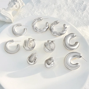 Polished silver metal hoop earring set in minimalist modern styles on white ceramic plate
