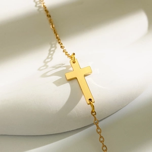 Detailaufnahme einer polierten Goldkreuz-Halskette auf einem weißen Skulpturständer