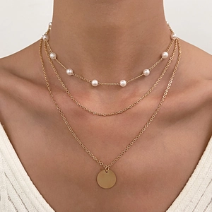 Detailed close-up of a three-layer gold necklace featuring pearls and a polished round pendant