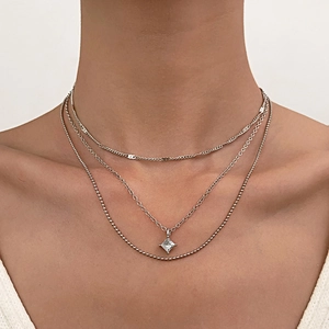 Detail of layered silver necklace showing a square zircon pendant and delicate beaded chain