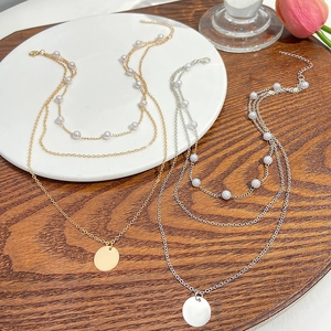 Close-up of layered necklace with faux pearls and round pendant on a ceramic dish