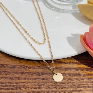 Detail of minimalist double-layer gold chain necklace with smooth round pendant on table