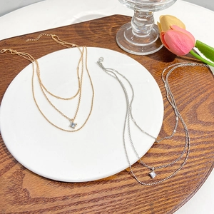 Detailed top view of layered gold and silver necklaces with a square gemstone pendant