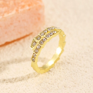 Detail of gold snake-shaped ring with pavé zircons on textured beige sand background