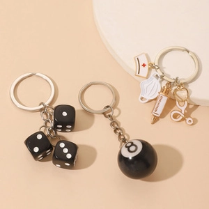 Detail of alloy keychains featuring dice, 8-ball, and medical charms on a beige background