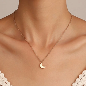 Detalle de un delicado collar con colgante de luna dorada en la clavícula de una mujer