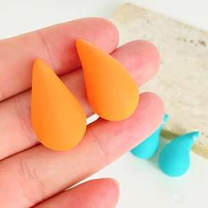 Close-up of bright orange waterdrop earrings with a matte frosted finish on hand
