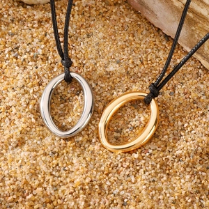 Close-up of gold and silver oval pendants with black cord on a natural sand background