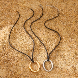 Detail view of gold and silver oval metal pendants on black cord necklaces over sand