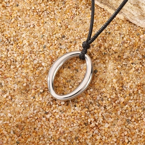 Detailed view of a silver polished oval pendant on a black cord over sand background