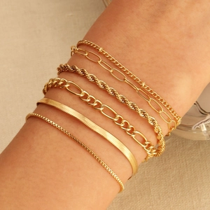 Détail de six bracelets dorés superposés comprenant des mailles serpent, figaro et gourmette