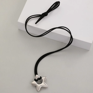 Détail d'un pendentif étoile argenté avec cordon noir sur un support géométrique blanc
