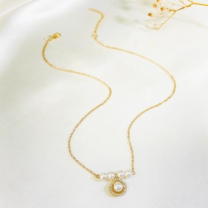 Macro detail of a golden shell pendant with a large pearl and sparkling pavé crystals