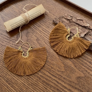 Pendientes bohemios de abanico con borlas y grabados dorados sobre fondo de madera rústica