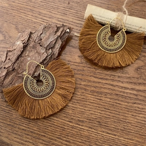 Detalle de pendientes bohemios con motivos calados dorados y borlas de algodón marrones