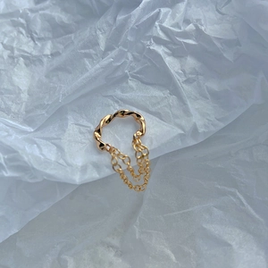 Detail eines goldenen Ear Cuff mit gedrehtem Design und feinen doppelten Kettenanhängern