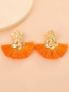 Detalle de pendientes boho en forma de abanico con flores doradas y borlas naranjas