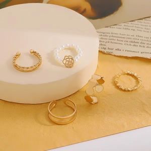 Detail of five gold rings featuring white faux pearls and hollow flower charms in stackable styles