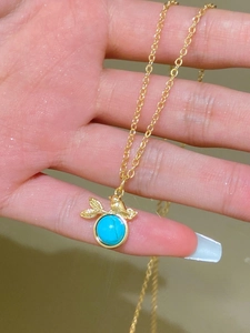 Close-up of gold bird and leaf necklace with turquoise blue stone held in hand for size