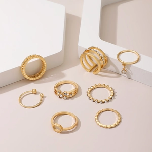 Detail of 8 gold alloy rings with rhinestones and textured bands on white stands