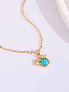 Macro detail of gold bird necklace featuring green turquoise stone and delicate leaf charms