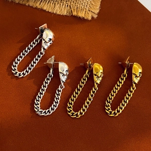 Detailansicht goldener und silberner Punk-Totenkopf-Ohrhänger auf strukturiertem Grund