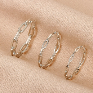 Detailed view of silver chain link stackable rings on champagne silk fabric background