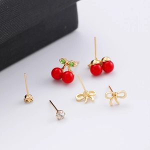 Macro detail of cherry stud earrings with red glossy finish and gold bow accents