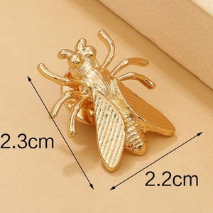Dettaglio spilla a forma di insetto dorato con misure 2,3 cm x 2,2 cm su base beige