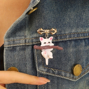 Détail d'une mignonne broche chat blanc avec nœud doré fixée sur une veste en jean