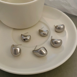 Close-up of six polished silver teardrop earrings displayed on a white ceramic plate